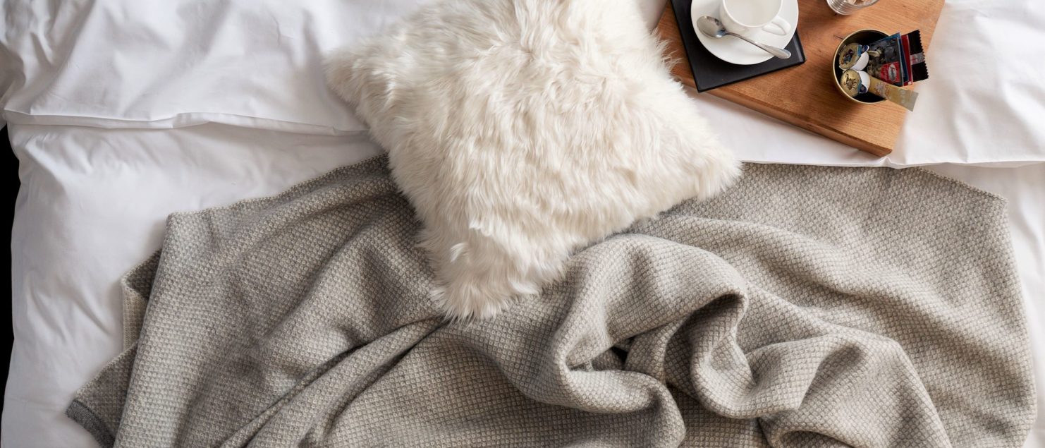 Tuwi white Fur Cushion and grey Alpaca wool Qori Throw on a bed